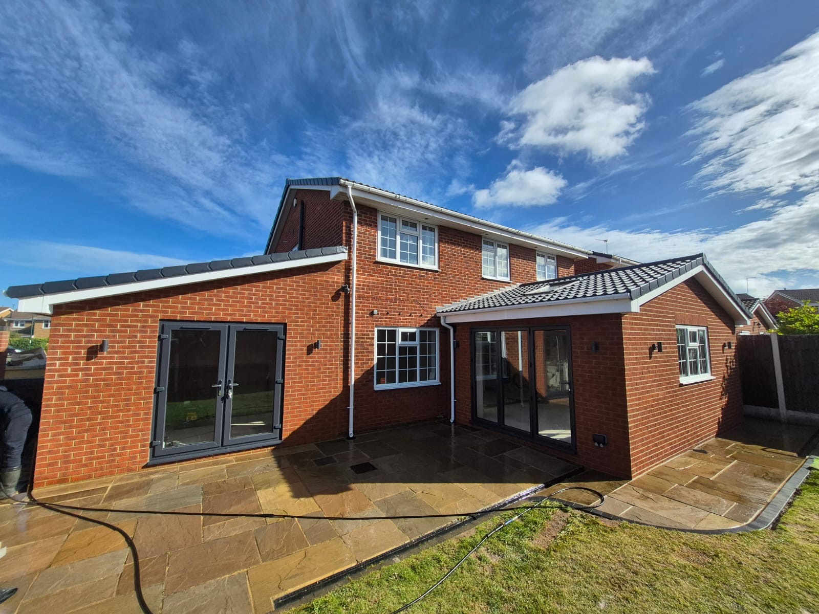 Two finished red-brick rear extensions either side of a house, with grey French doors, black bifolds and a new stone patio