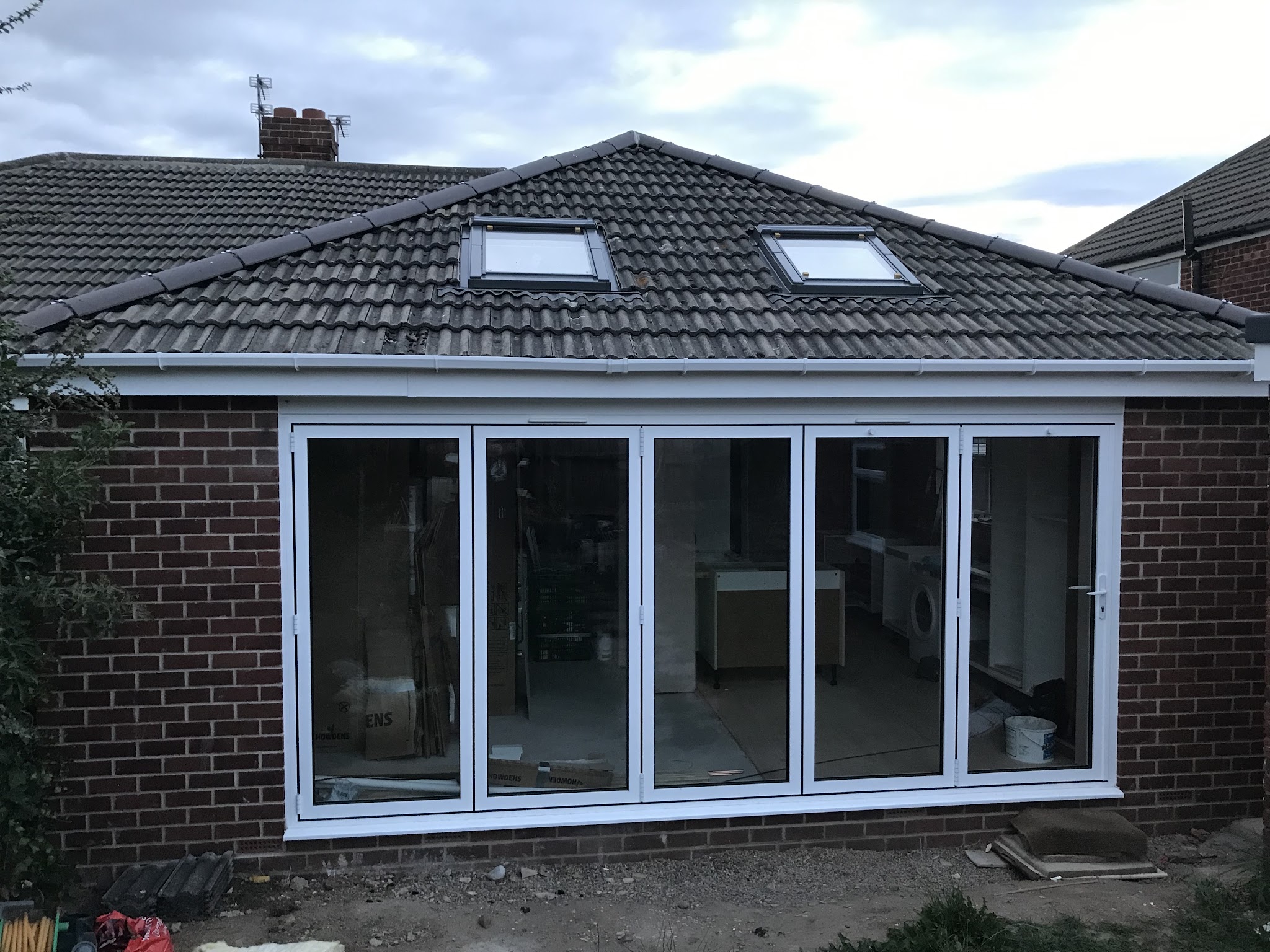 A newly built single-storey extension with a hipped tiled roof, two roof windows and five-panel white bifold doors