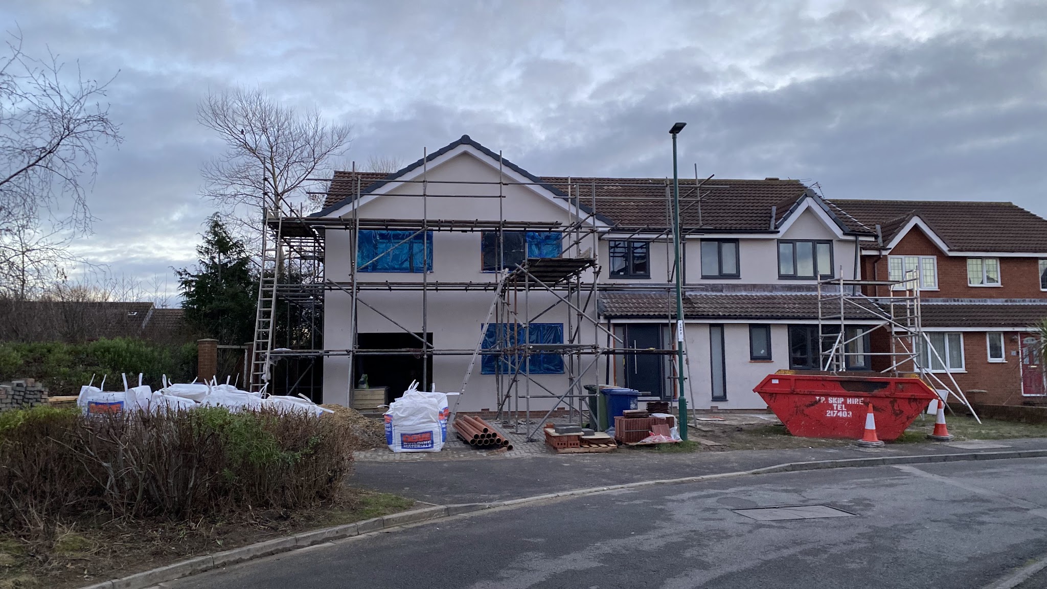 The extension and the original house rendered in off-white, with scaffolding still up and windows protected